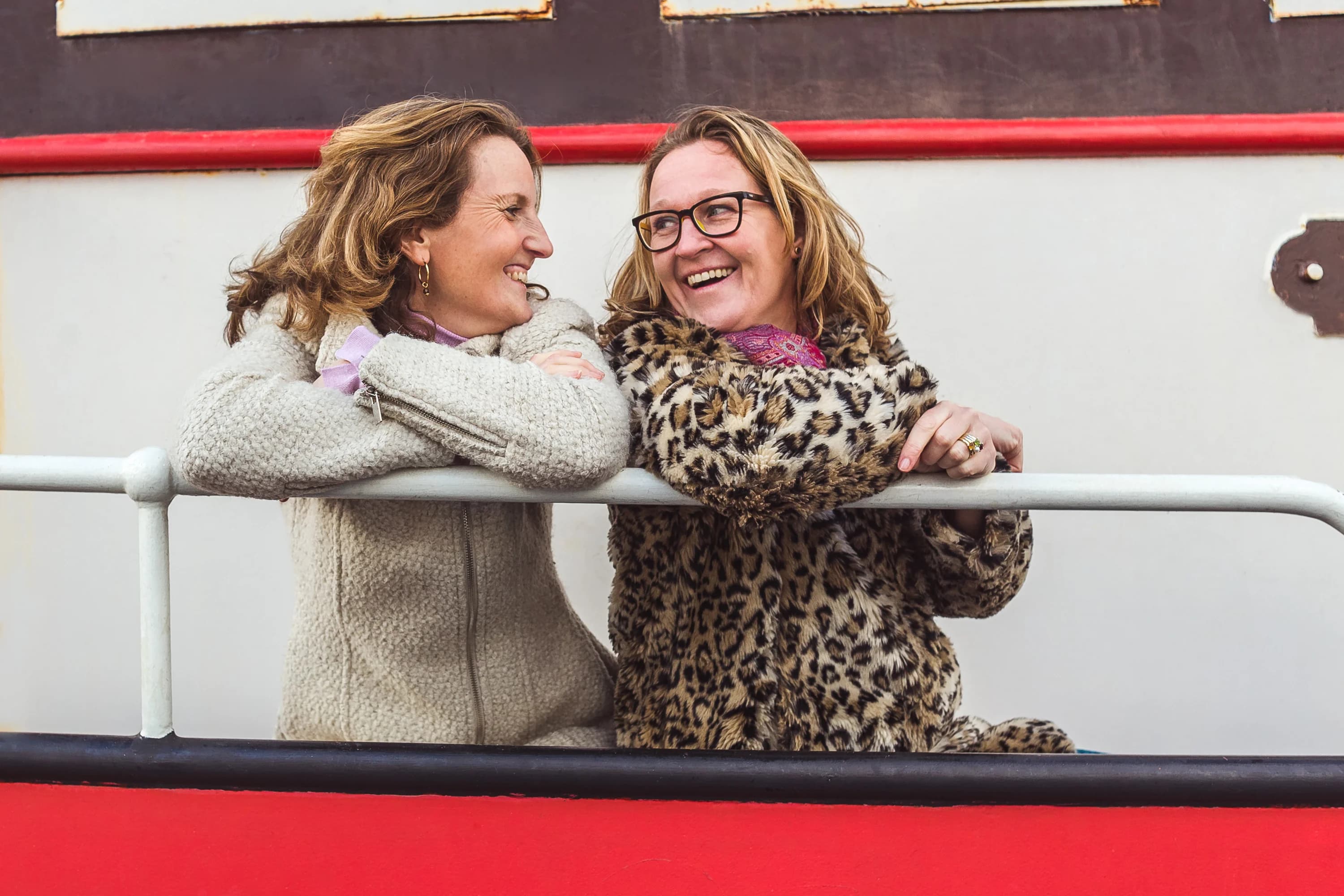 Twee vrouwen lachen ontspannen samen tijdens een zakelijke fotoshoot.